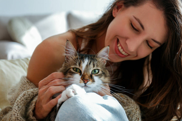 Portrait of young woman holding cute siberian cat with green eyes. Female hugging her cute long hair kitty. Background, copy space, close up. Adorable domestic pet concept. - Photo, Image