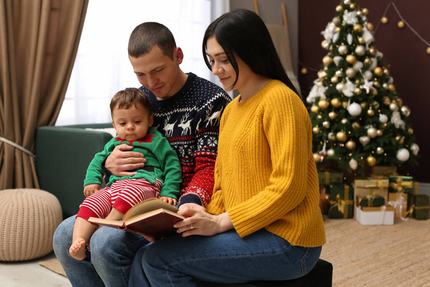 Parents reading book to their cute son in room decorated for Christmas - Foto, imagen