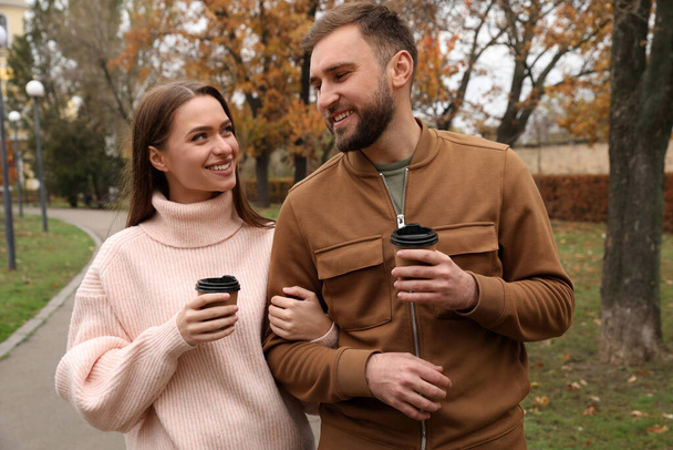 Happy couple wearing stylish clothes with cups of coffee in autumn park - Photo, image