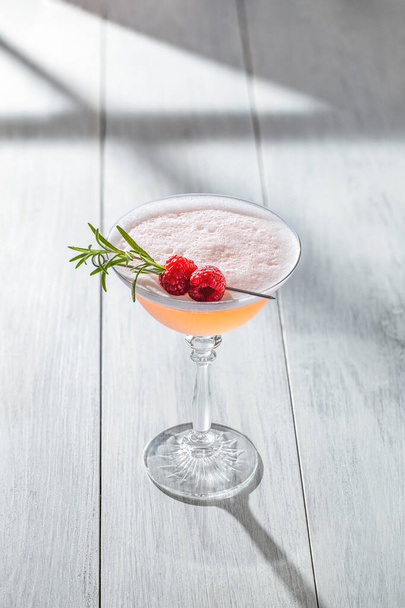 Clover Club Cocktail, ein säuerliches Getränk mit Gin, Himbeeren und eiweißem Schaum auf heller Betonoberfläche in Fensternähe mit sonniger Hintergrundbeleuchtung. - Foto, Bild