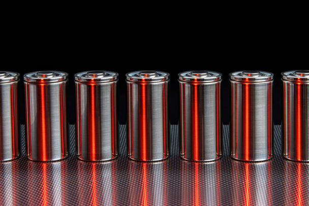 A consignment of new modern high-capacity lithium-ion cells. A prototype of new batteries on a steel surface illuminated with red light on a black background - Zdjęcie, obraz
