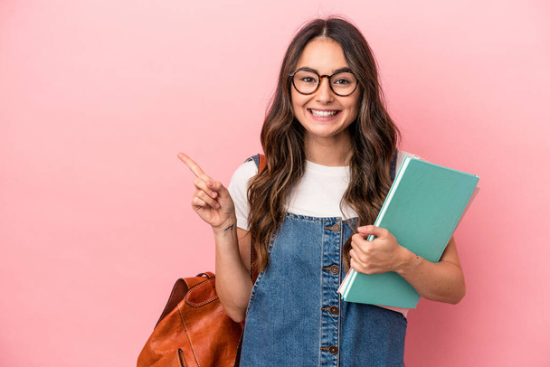 Young caucasian student woman isolated on pink background smiling and pointing aside, showing something at blank space. - Photo, Image