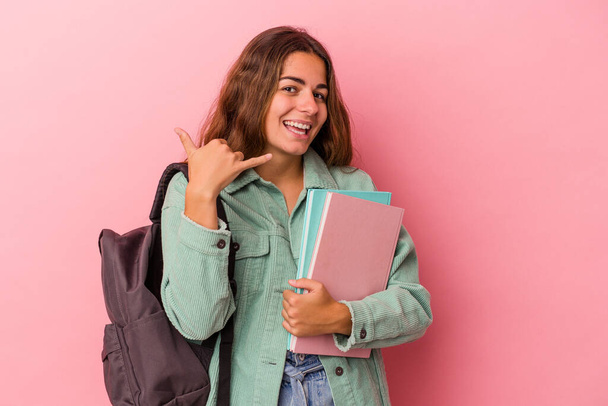Jovem estudante caucasiana segurando livros isolados em fundo rosa mostrando um gesto de chamada telefônica móvel com os dedos. - Foto, Imagem
