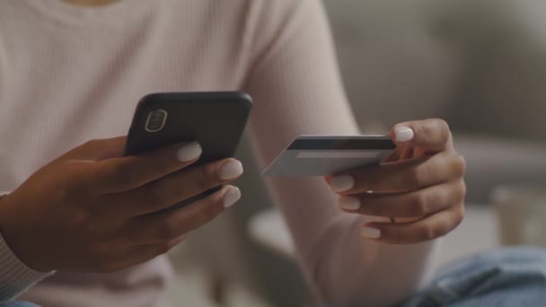 Koncepcja bankowości mobilnej. Nierozpoznawalna czarna kobieta trzymająca smartfona i kartę kredytową oraz dokonująca płatności w internecie - Materiał filmowy, wideo