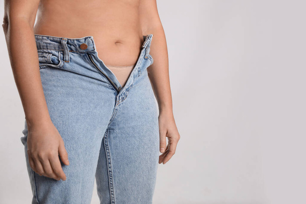 Woman in unfit jeans on light background, closeup. Space for text - Φωτογραφία, εικόνα