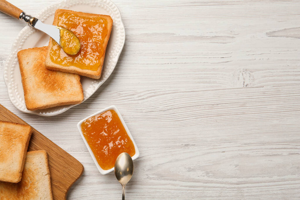 Toasts and orange jam served on white wooden table, flat lay. Space for text - Foto, afbeelding