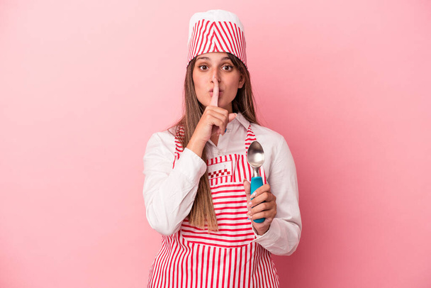 Young ice cream maker woman holding spoon isolated on pink background keeping a secret or asking for silence. - Photo, Image