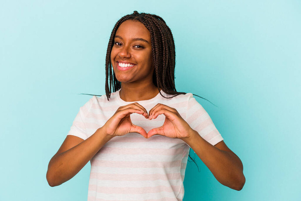 Joven mujer afroamericana aislada sobre fondo azul sonriendo y mostrando una forma de corazón con las manos. - Foto, imagen