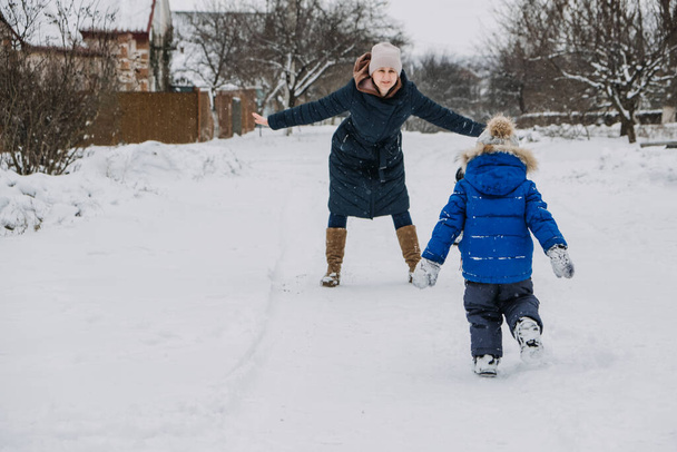 Outdoor family activities for happy winter holidays. Happy mother and two sons playing snowballs on snowy street in suburb. Happy family on winter weekend, Christmas holidays - Photo, Image