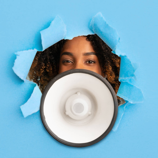 Great shopping offer. Black woman yelling into megaphone, announcing big sale through hole in torn blue paper - Photo, Image