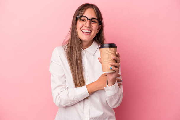 Young business caucasian woman holding a take away isolated on pink background laughing and having fun. - Photo, Image
