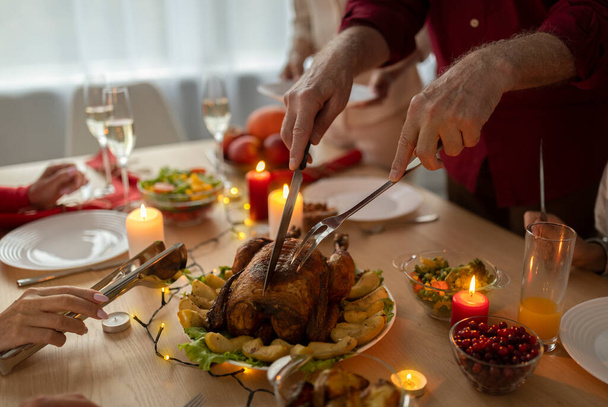 Unrecognizable senior man cutting roasted Christmas turkey, celebrating Xmas with his multi generation family at home - Фото, изображение