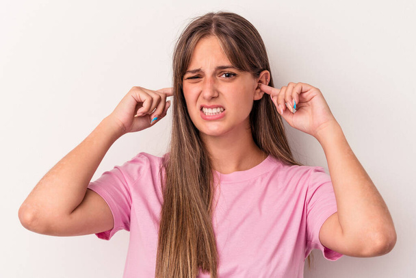 Mujer caucásica joven aislada sobre fondo blanco cubriendo las orejas con los dedos, estresada y desesperada por un ambiente ruidoso. - Foto, imagen