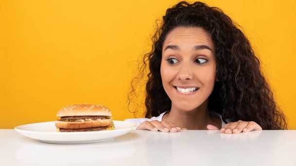 空腹の女性はハンバーガーのテーブルをのぞき見見て - 写真・画像