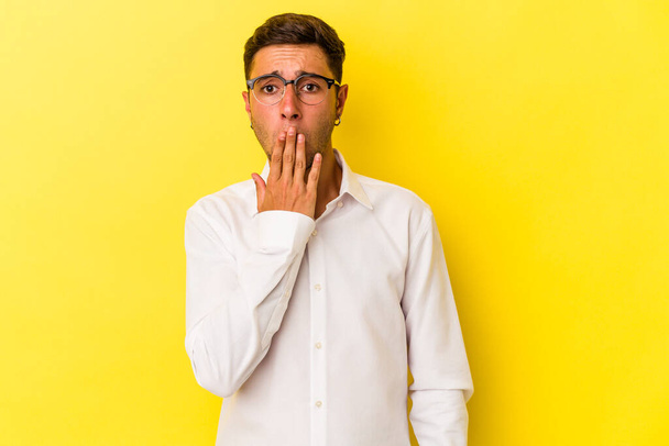 Young caucasian man with tattoos isolated on yellow background  shocked, covering mouth with hands, anxious to discover something new. - 写真・画像