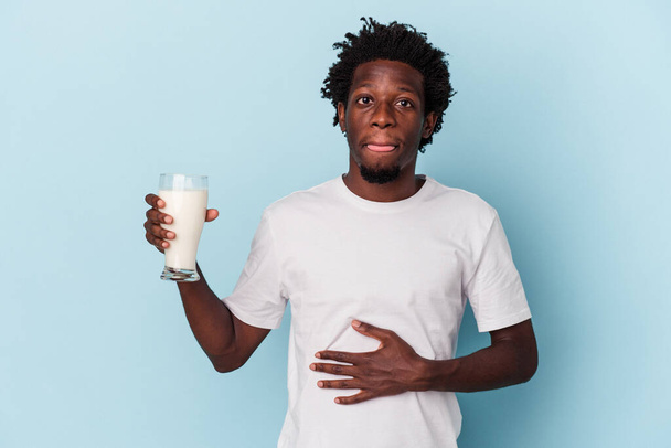 Mavi arka planda süt bardağı tutan genç Afrikalı Amerikalı adam. - Fotoğraf, Görsel