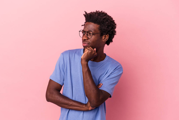 Jovem afro-americano isolado sobre fundo rosa confuso, sente-se duvidoso e inseguro. - Foto, Imagem