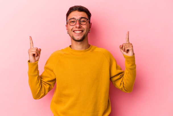 Young caucasian man with tattoos isolated on yellow background  indicates with both fore fingers up showing a blank space. - Photo, Image
