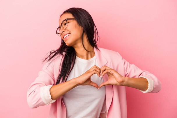 fiatal latin nő elszigetelt rózsaszín háttér mosolygó és mutató szív alakú kezek. - Fotó, kép