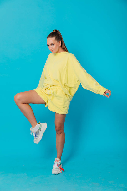 bela mulher em sportswear amarelo em um fundo azul - Foto, Imagem