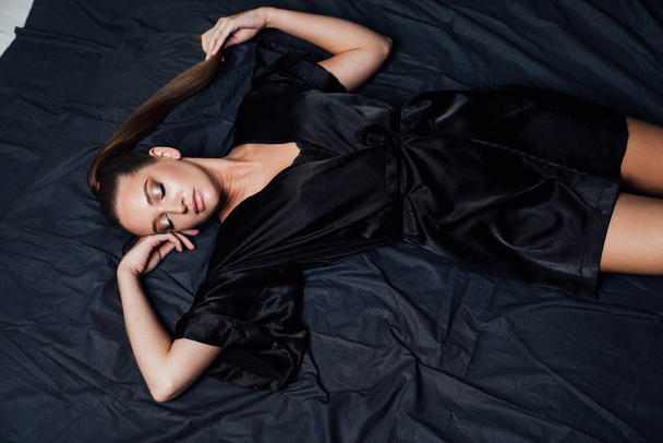 portrait of a beautiful woman in black linen on a bed in the bedroom - Zdjęcie, obraz