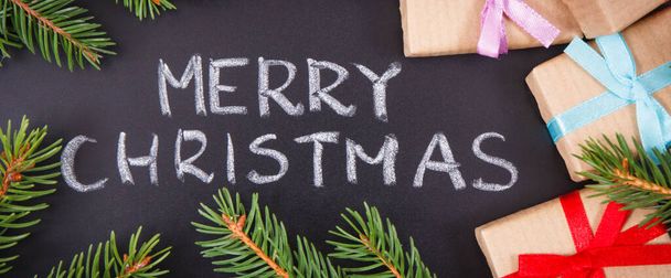 碑文メリークリスマス,黒の背景にリボンと緑のトウヒの枝で包まれた贈り物.クリスマスの時間の装飾 - 写真・画像
