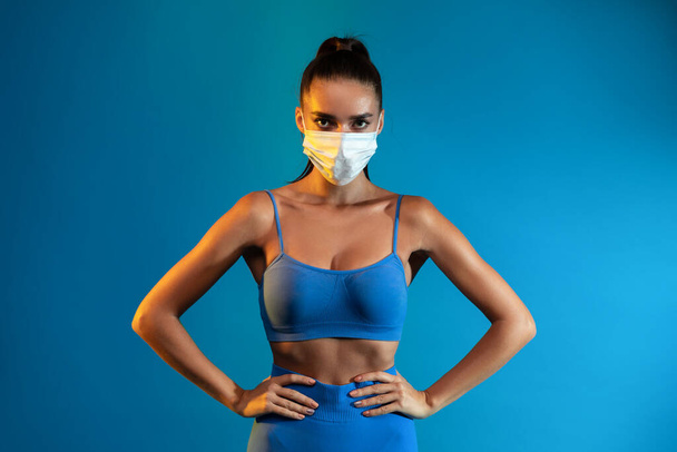 Sporty Lady Wearing Protective Face Mask Over Blue Studio Background - Фото, изображение