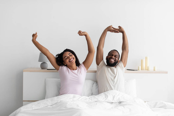 Happy millennial black husband and wife woke up, stretching bodies on white bed - Fotoğraf, Görsel