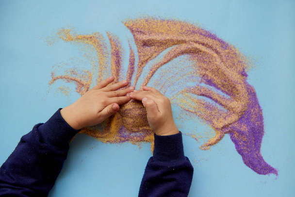 Sviluppo di capacità motorie fini per bambini. Bambino gioca con sabbia colorata. Occupazione creativa dei bambini. Vista dall'alto. Copia spazio. - Foto, immagini