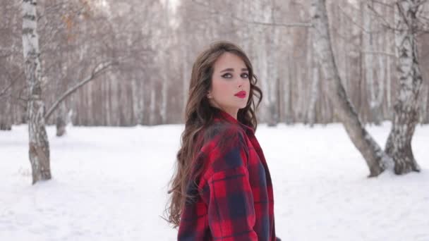 Mujer joven con el pelo ondulado de pie y la cara conmovedora en el bosque de invierno - Metraje, vídeo