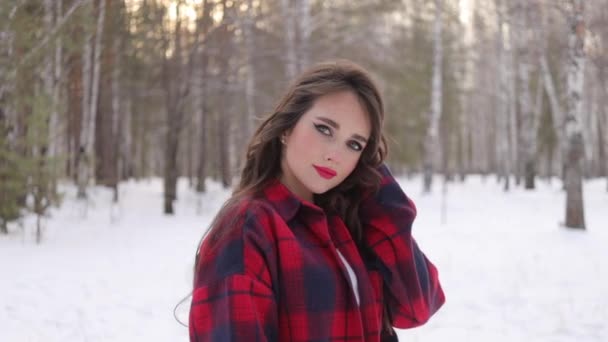 Νεαρή γυναίκα με κυματιστά μαλλιά στέκεται και συγκινητικό πρόσωπο στο δάσος του χειμώνα - Πλάνα, βίντεο