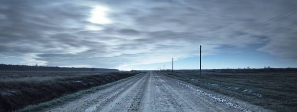 Illuminated rural road through the fields. Blue light. Electricity line. Dramatic twilight sky, moonrise. Atmospheric landscape. Panoramic view, copy space, art. Dangerous driving, loneliness concepts - Photo, Image