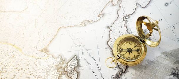 Goldener Kompass im Retro-Stil (Sonnenuhr) und alte weiße Seekarte in Nahaufnahme. Vintage-Stillleben. Segelzubehör. Thema Reisen und Navigation - Foto, Bild