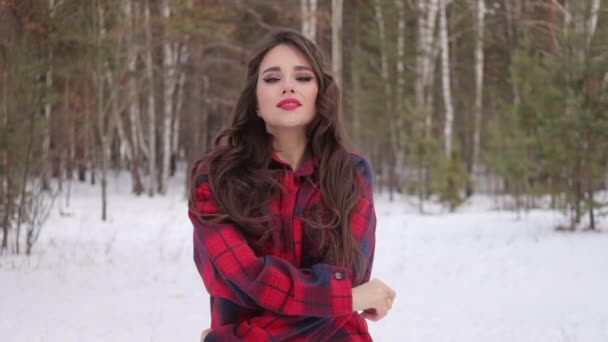 Giovane donna con capelli ondulati in piedi e faccia toccante nella foresta invernale - Filmati, video