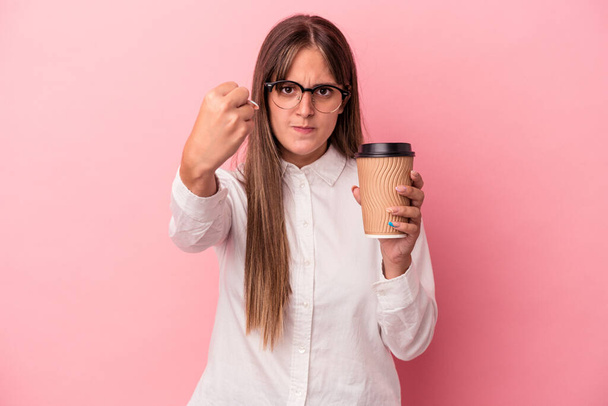 Young business caucasian woman holding a take away isolated on pink background showing fist to camera, aggressive facial expression. - Photo, Image