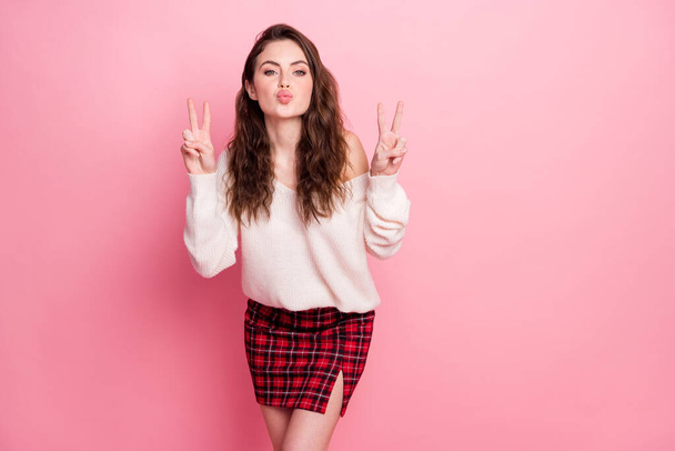 Photo of adorable young girl kiss lips fingers show v-sign wear sweater isolated on pink color background - 写真・画像