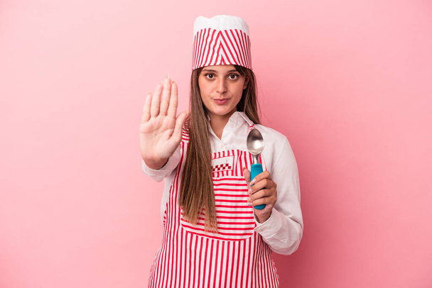 若いですアイスクリームメーカー女性保持スプーンピンクの背景に隔離されたスタンドでアウトストップサインを示す、あなたを防ぎます. - 写真・画像
