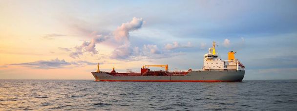 Großer grauer Tanker, der bei Sonnenuntergang vom Europort aus auf offener See unterwegs ist. Bunte Abendwolken. Rotterdam, Niederlande. Logistik, Handel, globales Kommunikationsthema - Foto, Bild