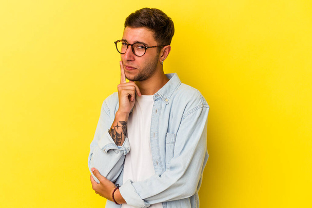 Young caucasian man with tattoos isolated on yellow background  contemplating, planning a strategy, thinking about the way of a business. - Fotografie, Obrázek
