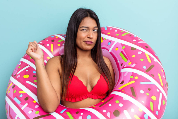 Young Venezuelan woman holding donut inflatable isolated on blue background confused, feels doubtful and unsure. - Photo, Image