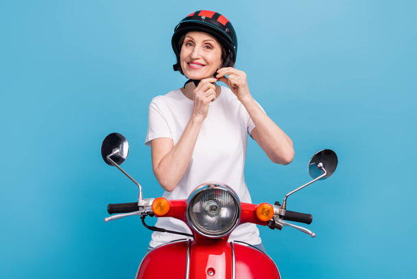 Portrait of attractive cheerful woman fixing helmet riding motor bike isolated over bright blue color background - Фото, зображення