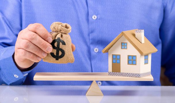 agent hold sack bag with dollar sign and home put on the scales with balance saving or loan for buy new house or plan business investment concept. - 写真・画像
