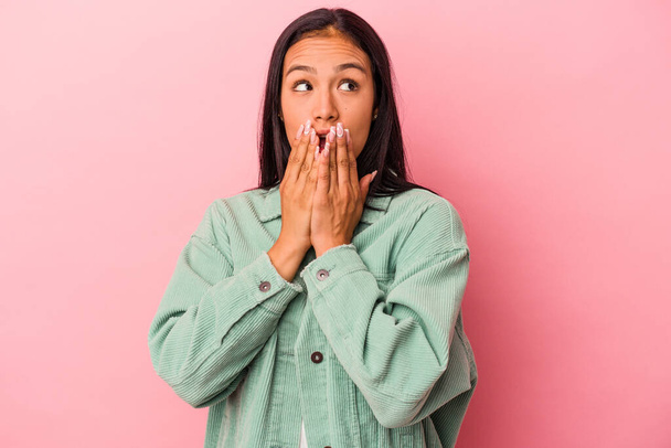 Jonge latijn vrouw geïsoleerd op roze achtergrond attent op zoek naar een kopieerruimte bedekken mond met de hand. - Foto, afbeelding