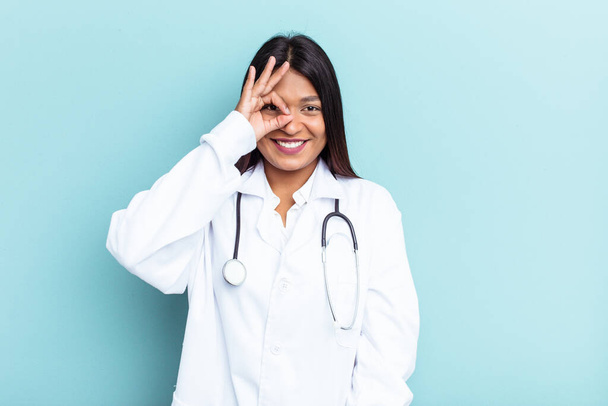 Young doctor Venezuelan woman isolated on blue background excited keeping ok gesture on eye. - Fotografie, Obrázek
