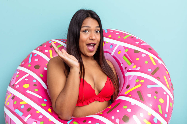 Young Venezuelan woman holding donut inflatable isolated on blue background surprised and shocked. - Fotografie, Obrázek