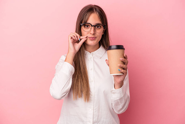 Young business caucasian woman holding a take away isolated on pink background with fingers on lips keeping a secret. - Photo, Image