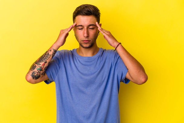 Young caucasian man with tattoos isolated on yellow background  touching temples and having headache. - Фото, изображение