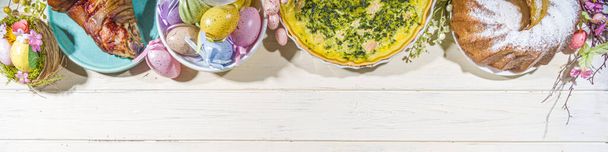 Праздничный ужин, пасхальный бранч. Традиционные пасхальные блюда на семейном столе - печеное мясо, пирог, весенний салат, кекс, цветные яйца, горячие булочки с крестом - Фото, изображение
