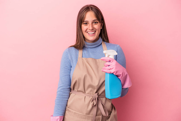 Fiatal kaukázusi tisztább nő gazdaság spray elszigetelt rózsaszín háttér boldog, mosolygós és vidám. - Fotó, kép