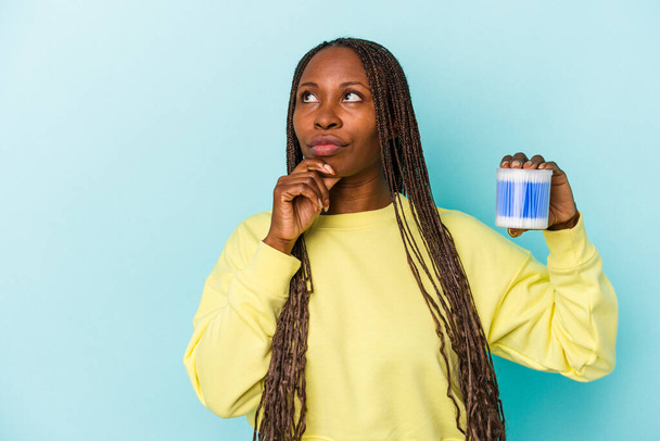 Young african american woman holding cotton bulls isolated on buds background looking sideways with doubtful and skeptical expression. - Photo, Image